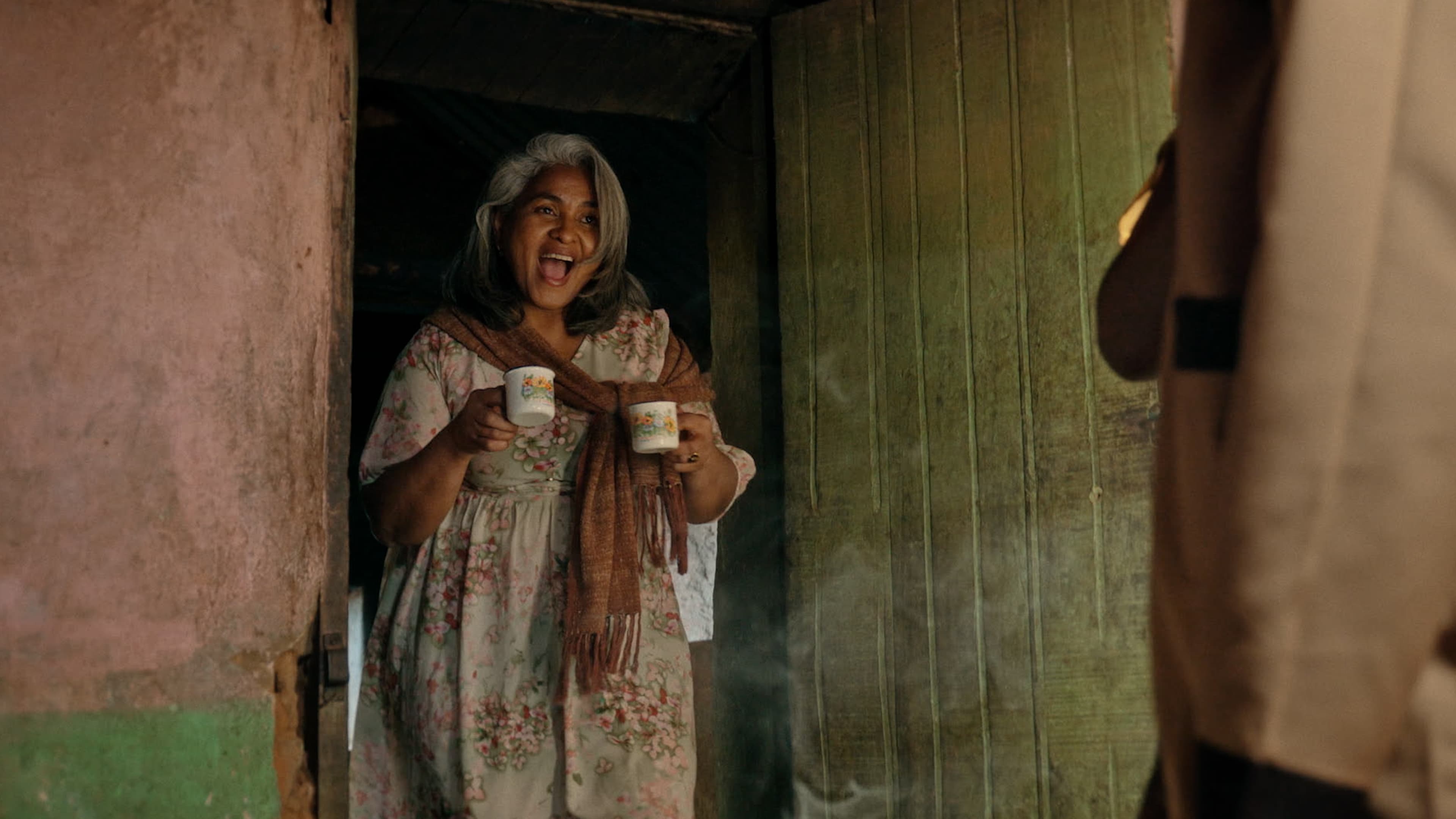 Une femme sourit sur le pas d'une porte, une tasse à la main